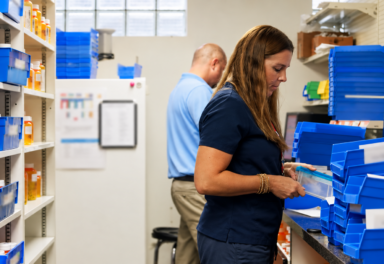 Pharmacy employees managing prescription workload among stacked pharmacy bins